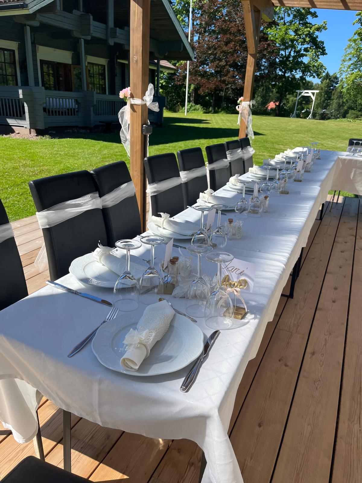 Katettu juhlapöytä pergolan alla, valkoiset liinat